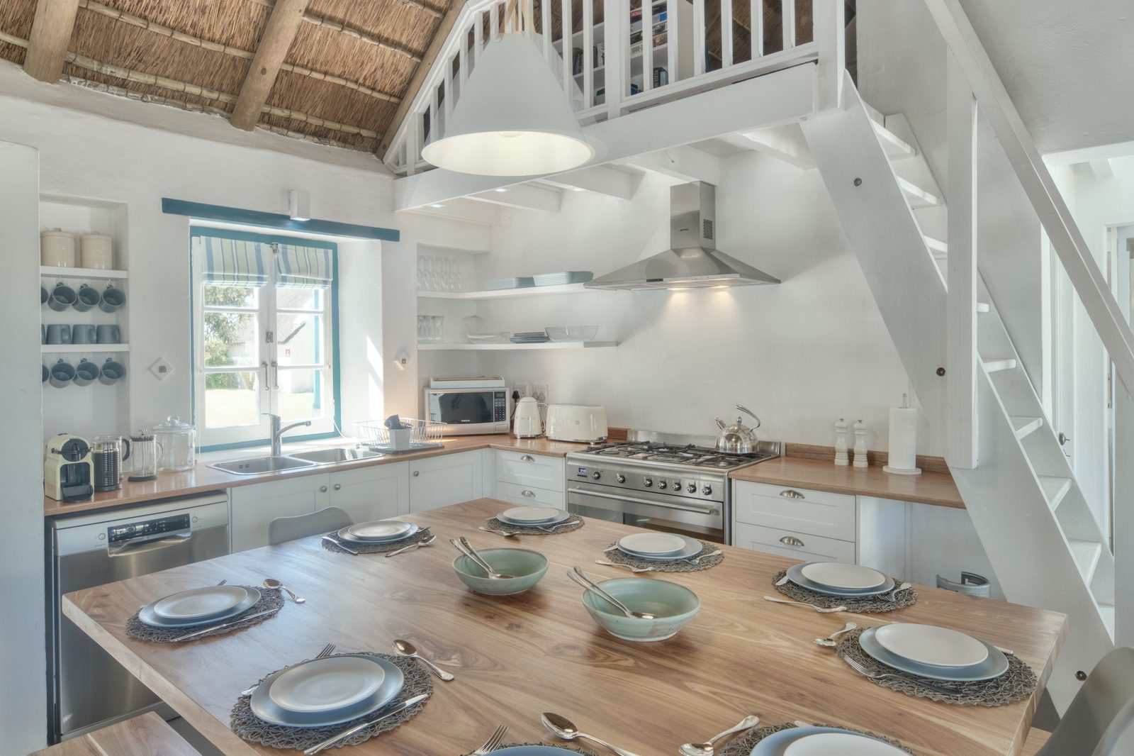 The long kitchen table at Cape Creek Retreat, laid for a full team beneath the thatch